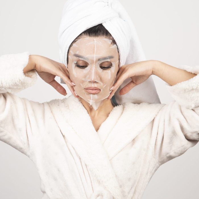 Portrait of young lady in bathrobe and towel on head while touching her face with facemask . High quality photo